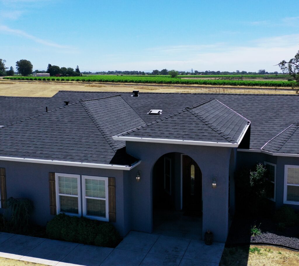 A well-maintained house with a black shingle roof installed by DavisRoofingGroup, set in a rural area of Galt, showcasing a neatly landscaped front yard and expansive fields in the background.